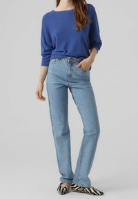 Pull bleu texturé à coupe ample, associé à un jean droit bleu clair et des ballerines rayées noires et blanches.