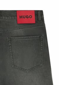 Zwarte denim jeans met een rode leren merkembleem met het label "HUGO," met één achterzak zichtbaar en gedetailleerde stiksels.