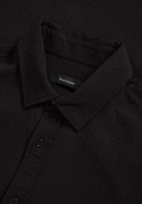 Melnas teksturētas krekls ar apkakli, uz kura priekšpuses ir zīmola "Matinique" uzlīme un melnas pogas.