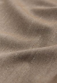 Gros plan sur un tissu beige avec de fines rayures diagonales et un tissage texturé montrant des plis subtils.