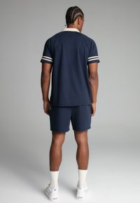 Navyblauwe polo met een crèmekleurige kraag, witte en marineblauwe gestreepte mouwen, gecombineerd met bijpassende marineblauwe shorts. Heeft een ontspannen pasvorm en een zachte textuur.