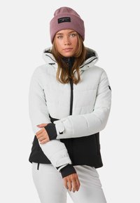 Giacca invernale imbottita di colore grigio chiaro e nero, con chiusura frontale con zip, cappuccio attaccato e polsini coordinati. Presenta una toppa con logo sul cappuccio.
