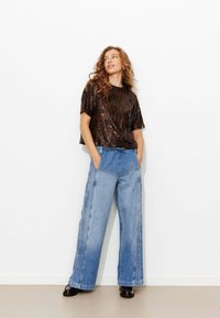 Haut court à manches courtes en sequins noirs associé à un pantalon ample en denim bleu clair avec des boutons-pression latéraux et une taille élastique.