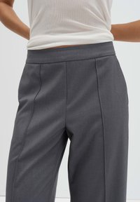 Op maat gemaakte grijze broek met een gladde stof, een wijd uitlopende pijp en plooien aan de voorkant, afgewerkt met een platte tailleband voor een strakke look.