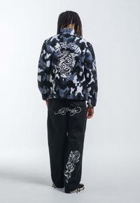 Fleecejacka med blå och svart kamouflagemönster, med en drake och ros grafik på baksidan; svarta byxor med vita blommönster.