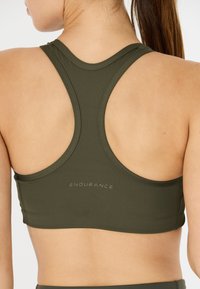 Oliivinvihreä urheiluliivit racerback-mallilla, jossa on teksturoitu kangas ja hillitty "ENDURANCE"-logo takana.