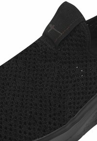 Chaussure noire à enfiler avec une tige en mesh texturé et tissé, et une semelle flexible. Comprend une languette en tissu pour un enfilage facile et un design minimaliste.