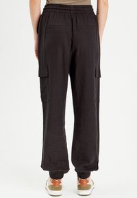 Pantalon cargo noir avec taille élastique, poches latérales et poignets élastiques. Le tissu semble léger et légèrement texturé.