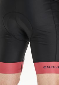 Svarta cykelshorts i stretchmaterial, med en svart vadderad insats och ett rött band vid fållen med "ENDURE" tryckt i svart.
