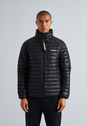 Doudoune noire avec col haut, design matelassé horizontal, poches zippées et logo sur la poitrine et la tirette.
