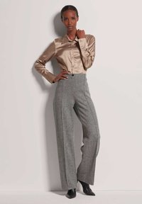 Satijnen beige blouse met lange mouwen en een puntige kraag, gecombineerd met hoge grijze woolen broeken met een wijde pijp en zwarte pumps met een puntige neus.