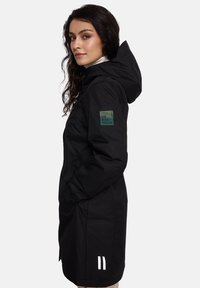 Juodas miesto parka su kapišonu, su žaliu lopu ant rankovės ir baltais akcentais briaunoje. Pagamintas iš lengvos, vandeniui atsparios medžiagos.