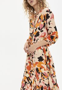 Bloemige jurk met oranje, roze en zwarte patronen op een lichte achtergrond, met knoopdetails enGathered cuffs.