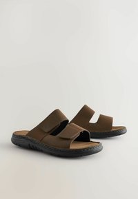 Sandales en cuir marron avec deux larges brides, ouverture au niveau des orteils et semelle en caoutchouc noir texturé. Semelle intérieure douce pour le confort.
