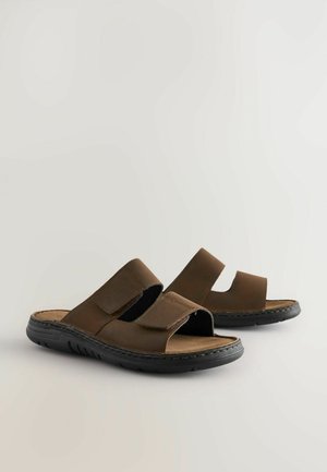 Brūni ādas slide sandales ar divām platiem sprādzēm, atvērtu purngalu un teksturētu melnu gumijas zoli. Mīksts zolītes ieliktnis ērtībai.