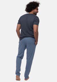 Navy T-Shirt mit kurzen Ärmeln, kombiniert mit gemusterten Schlafanzughosen in Blau und Weiß, die ein Rautenmuster und seitliche Taschen aufweisen.