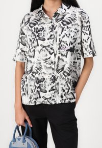 Chemise à manches courtes avec motifs abstraits en noir et blanc, fabriquée en tissu léger, dotée d'une poche poitrine et d'un style boutonné.