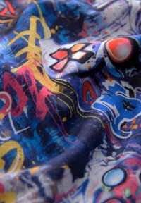 Farbiger Stoff mit einer Mischung aus blauen, roten, gelben und weißen abstrakten Mustern, die eine strukturierte Oberfläche und geschichtete Designs aufweisen.