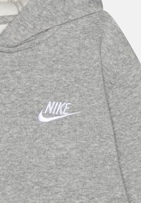 Grå huvtröja med mjuk textur, med en vit broderad "Nike"-logotyp på vänster bröst. Enkel design, justerbar huva.