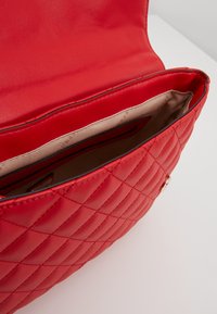 Sac à bandoulière en cuir matelassé rouge ouvert, montrant une doublure intérieure en tissu beige et des poches.