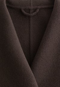 Brauner Wollmantel aus einem weichen, strukturierten Stoff mit einem Reverskragen und einer Schlaufenverzierung am Halsauschnitt. Sauberes Design mit dezenten Nähten.