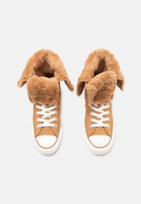 Sneaker alte marroni in suede con foderatura in pelliccia morbida e colletto pieghevole. Lacci bianchi e suole in gomma con punta arrotondata.