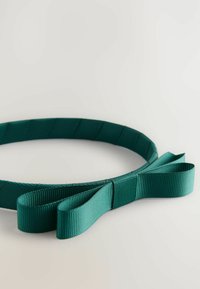 Turkos band med rosett, placerad mot en ljus bakgrund som visar dess textur och design.