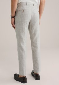 Lichtgrijze linnen broek met een subtiele streeppatroon, twee achterzakken en bruine knopenaccenten. De schoenen zijn zwart en met een platte hak.
