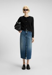 Svart stickad cardigan med guldknappar, högmidjade blå jeanskjol, svart läderväska och glansiga platåskor. Texturerade tyger, modern design.