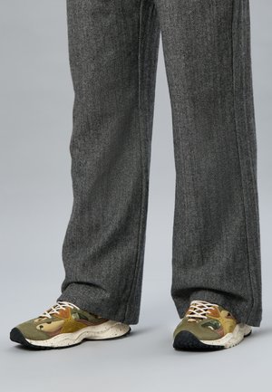 Pantalon gris à jambes larges en chevron, associé à des baskets vertes et marron à motif camouflage, lacets blancs et semelles tachetées.