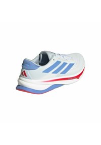 Weißer Laufschuh mit blauen Streifen und roten Akzenten, beschriftet mit "Dreamstrike", ausgestattet mit einer dicken gepolsterten Sohle und Schnürdesign.