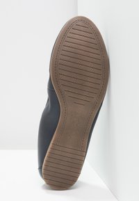 Svart skosula med texturerat gummi grepp, med horisontella och vertikala mönster samt en slät kant, vilande mot en vit bakgrund.