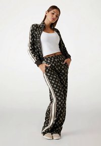 Schwarz-weiß gemusterter Trainingsanzug mit passender Jacke und Hose. Die Jacke verfügt über einen Reißverschluss und kontrastierende seitliche Streifen; die Hose hat Taschen.