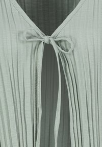 Light green pleated fabric with a tie closure at the front. Soft texture and a v-neck design, featuring delicate stitches along the edges.