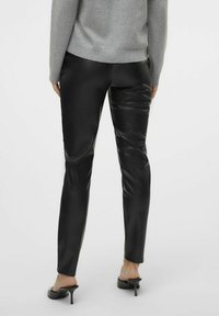 Pantalons en simili cuir noir avec une texture lisse, une coupe ajustée et de subtils détails de froissage. Portés avec un pull en tricot gris.