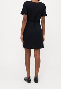 Sort kjole med korte ærmer og løs pasform, med en indsnævret talje, glat stof og en knælængde, kombineret med sorte flade sko.
