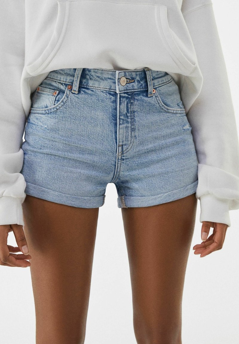 Ljust blå denimshorts med hög midja, uppvikt fåll och femficksdesign. Har metallknapp och dragkedjestängning.