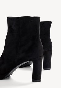 Bottines en daim noir avec une texture lisse, dotées d'un talon carré et d'un design minimaliste. Détails subtils avec un logo discret à l'arrière.