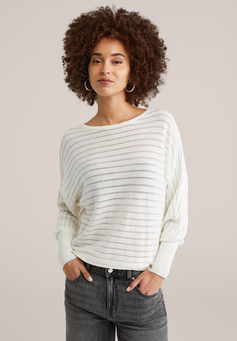 Pull à rayures blanches à coupe ample, avec des poignets côtelés et un col large, porté avec un jean gris foncé taille haute.
