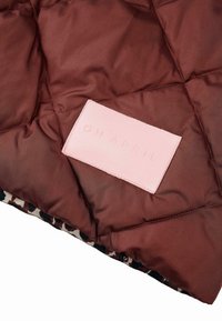 Hnedý prešívaný pufér s jemnou textúrou. Obsahuje svetloružovú koženú nálepku s nápisom "OH APRIL." Interiér má vzor leopardieho tlače.