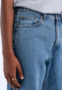 Lichtblauwe denim jeans met een relaxte pasvorm, voorzien van een klassiek vijf-pocket ontwerp, messingen hardware en subtiele vervagingdetails.