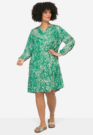 Robe verte à motifs avec des manches longues, un décolleté en V et une jupe évasée. Le design présente des formes abstraites dans des couleurs claires contrastantes.