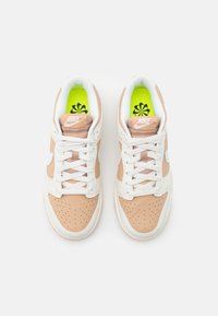 Sneakers Nike con tomaia in pelle bianca e beige chiaro, punta traforata, lacci bianchi e soletta verde brillante con motivo floreale.