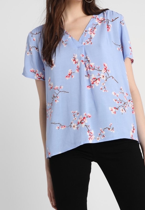 Blusa floral azul con mangas cortas, con un escote en V y un corte holgado. Patrones de flores rosadas y ramas en todo el diseño.