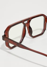 Gafas rectangulares de tonalidad marrón con un marco grueso, que presentan lentes transparentes, diseño geométrico y un acabado brillante en las patillas.