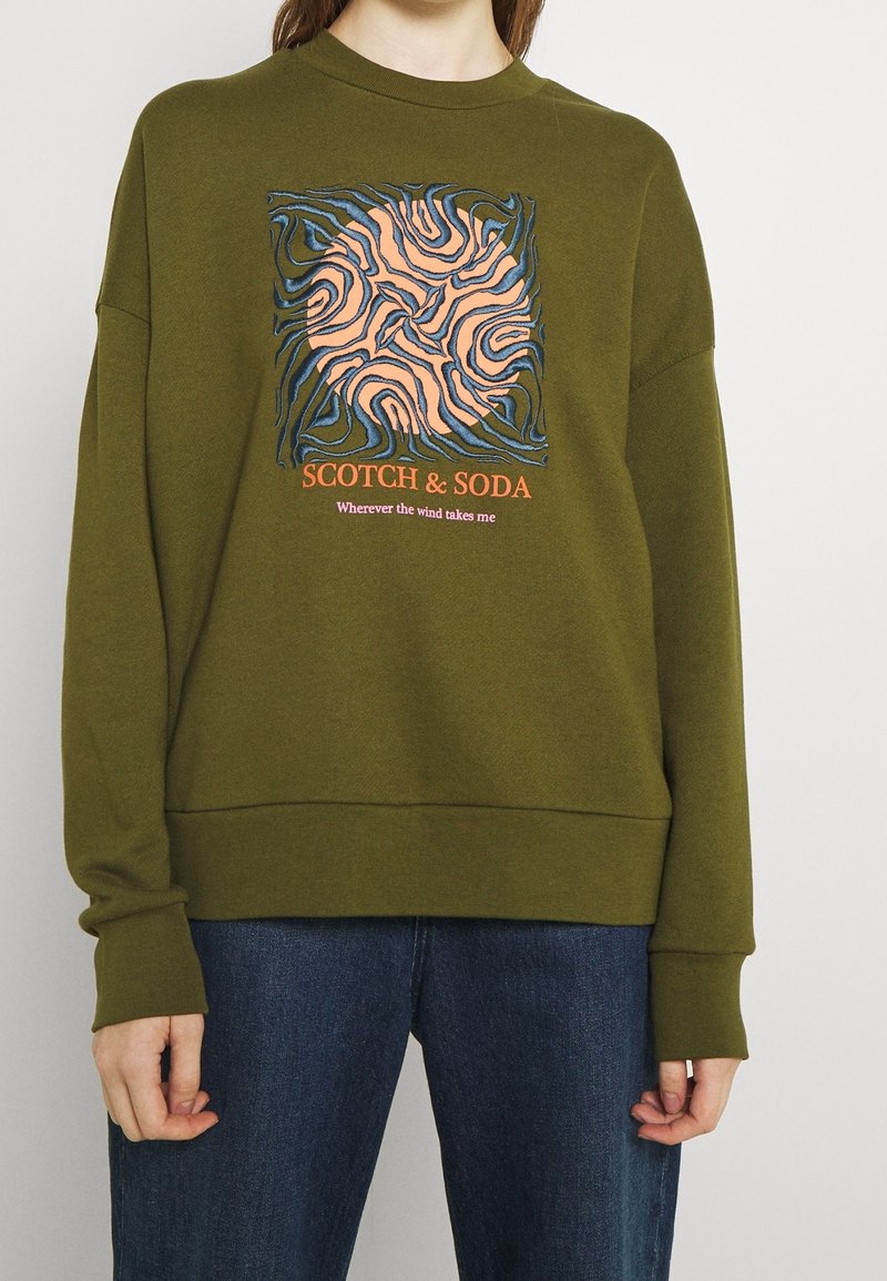 Oliwkowy sweatshirt z okrągłym dekoltem, z wielokolorowym abstrakcyjnym wzorem i napisem "SCOTCH & SODA" na środku.