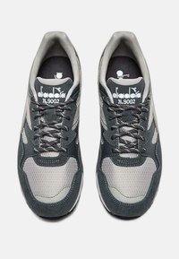 Scarpe da ginnastica grigie e nere con materiali in rete e suede, punta arrotondata, colletto imbottito e lacci multicolori, con un logo sulla linguetta.