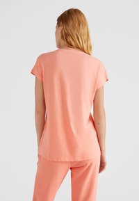 Lekka koszulka z krótkim rękawem z miękkiej koralowej tkaniny, z okrągłym dekoltem i luźnym krojem. W zestawie ze spodniami w tym samym kolorze.
