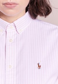 Ljusrosa randig kavajskjorta med ett litet broderat hästlogo på vänster bröst, vita knappar och klassisk krage.