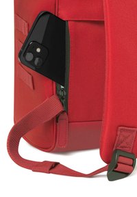 Rode stoffen tas met een ritsvak, waarin een zwarte smartphone zichtbaar is. Beschikt over een stevige schouderriem en een gestructureerd materiaal.